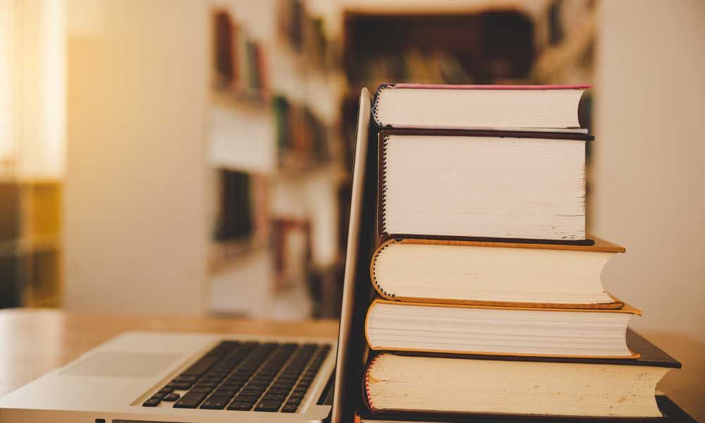 Books in a library with an open laptop.