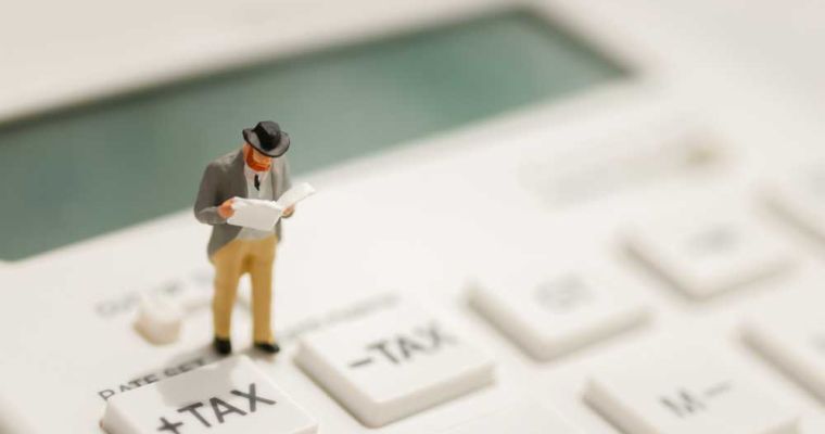 Miniature businessman stand reading on tax button of calculator