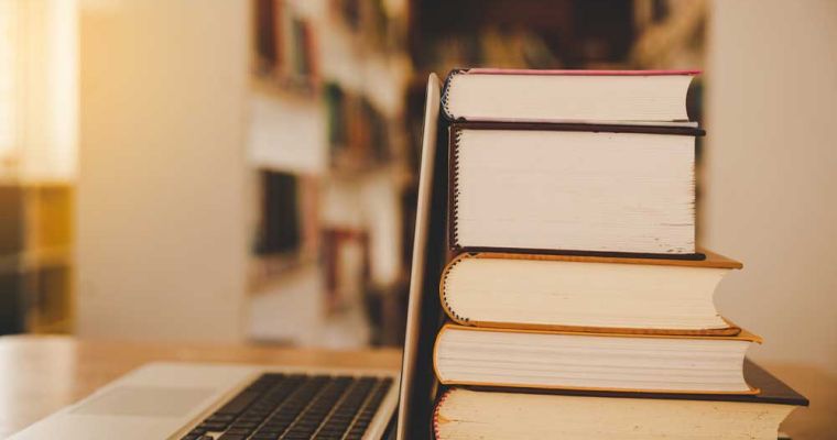 Books in a library with an open laptop.
